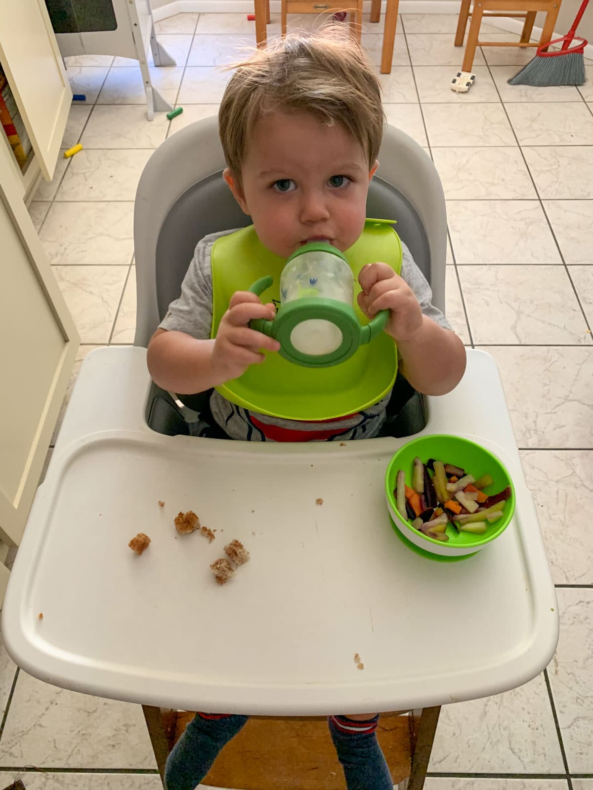 toddler drinking milk and eating veggie mix in a bowl with peanut butter and jelly