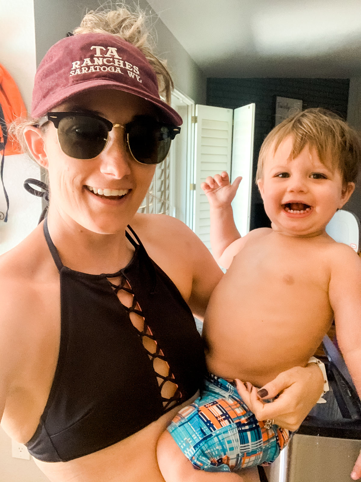 mom with swim suit top on and vvisor holding toddler both are smiling