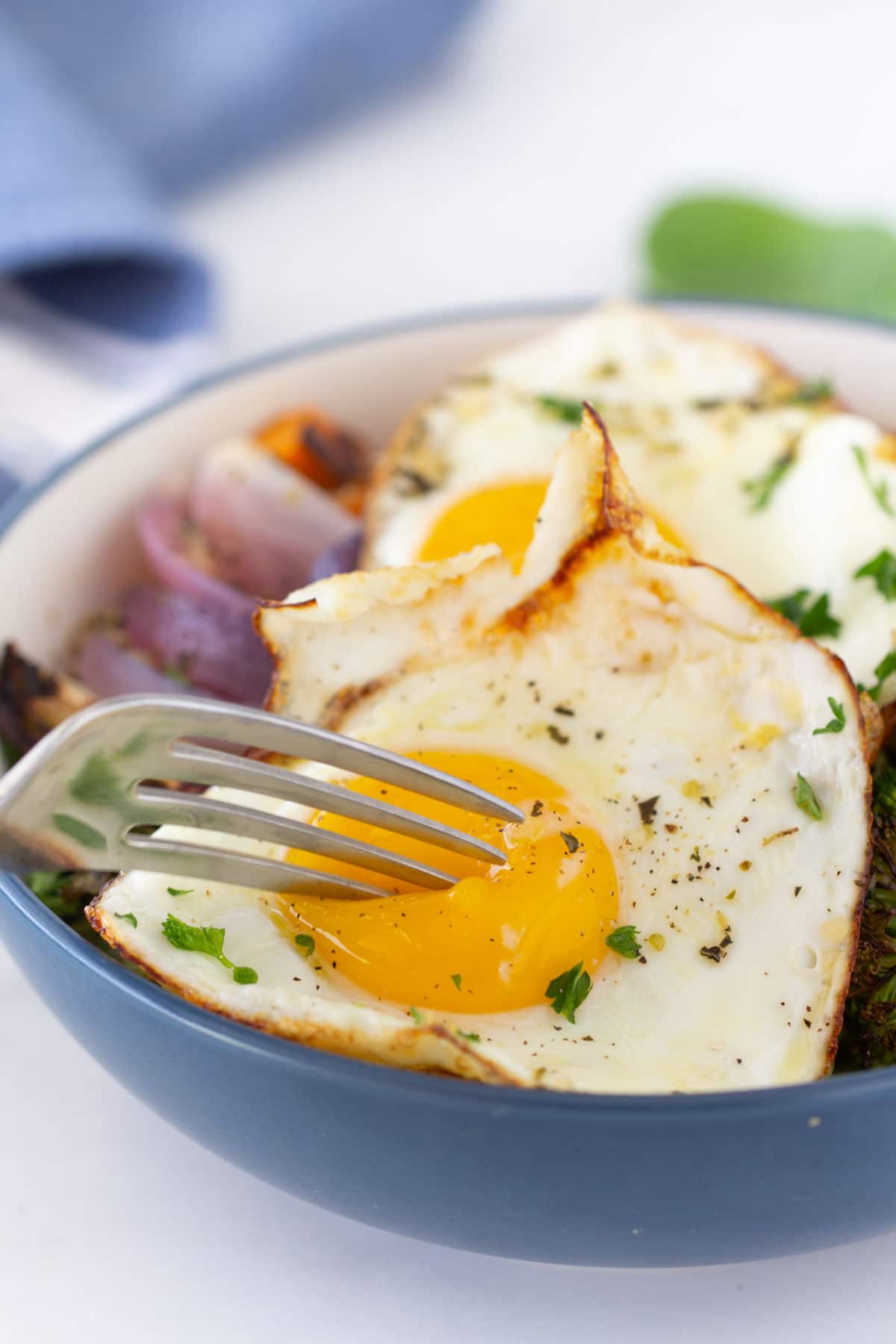 fried eggs on top of roasted veggies with fork cutting through