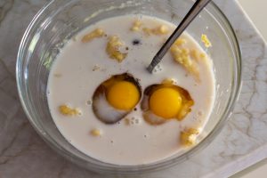 Glass bowl of wet ingredients mixed with rolled oats and mashed bananas for healthy oatmeal banana bread batter