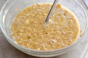 Mixing bowl with mashed bananas, oats, and wet ingredients being stirred together to make healthy oatmeal banana bread batter.