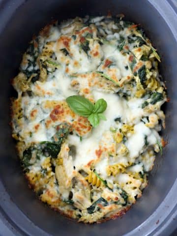 Slow cooker pesto chicken pasta topped with melted mozzarella cheese after broiling until golden.