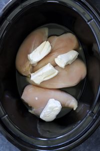 Crockpot crack chicken ingredients with raw chicken breasts, cream cheese, and broth in slow cooker