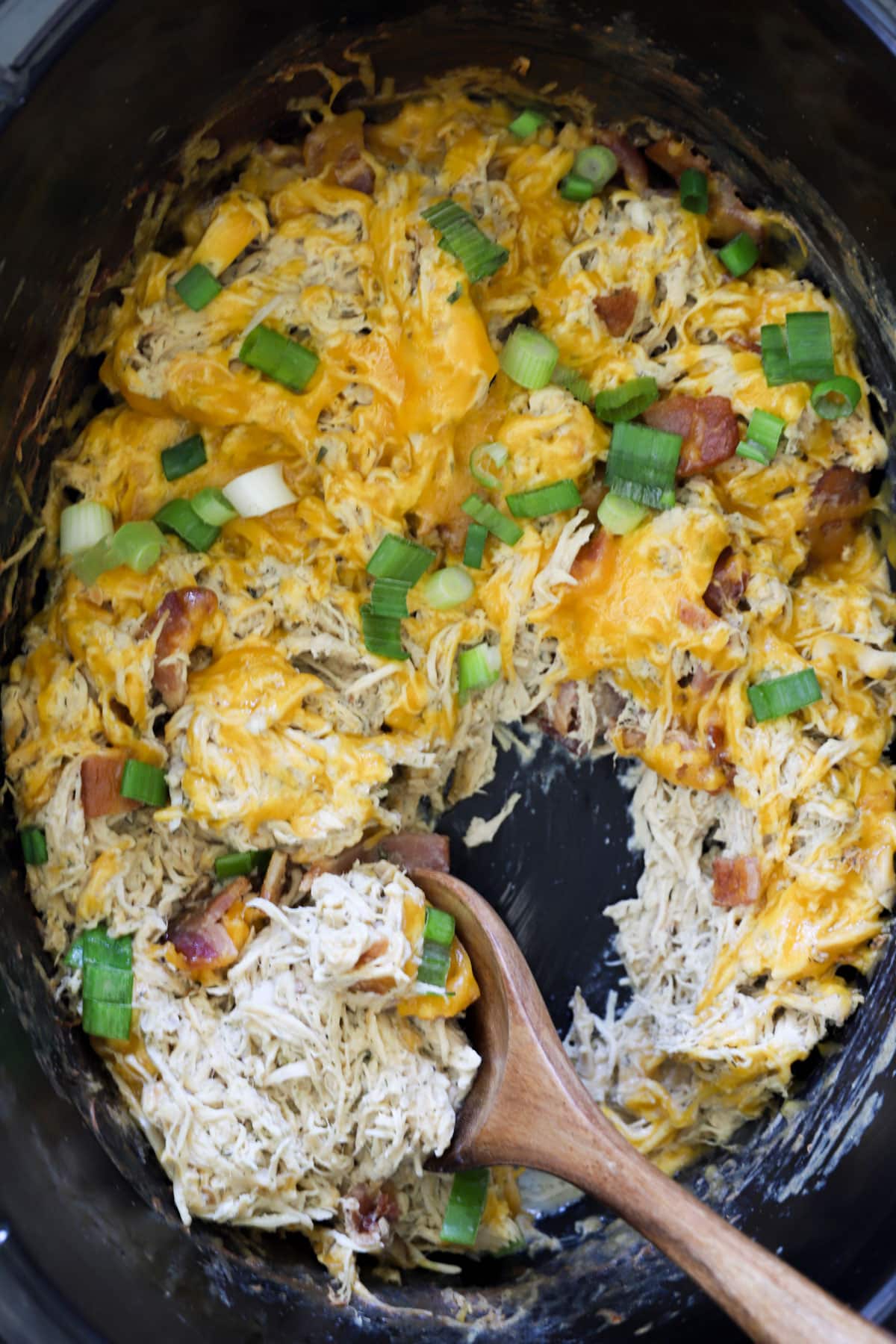 Spoonful of creamy crockpot crack chicken with bacon and melted cheddar in slow cooker