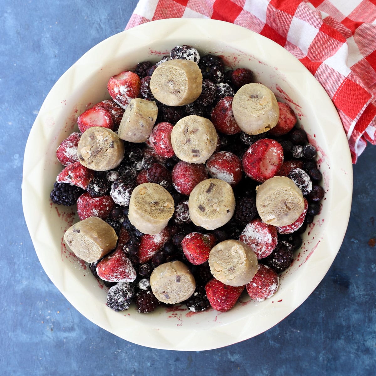 Rounds of ready-to-bake cookie dough placed over frozen berries in a baking dish before baking