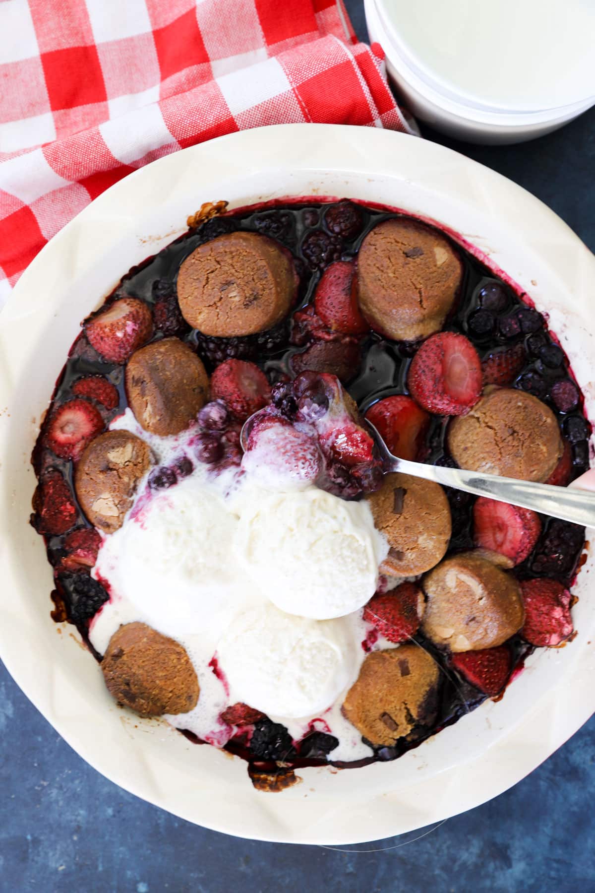 Cookie berry crumble topped with two scoops of melting vanilla ice cream and a serving spoon