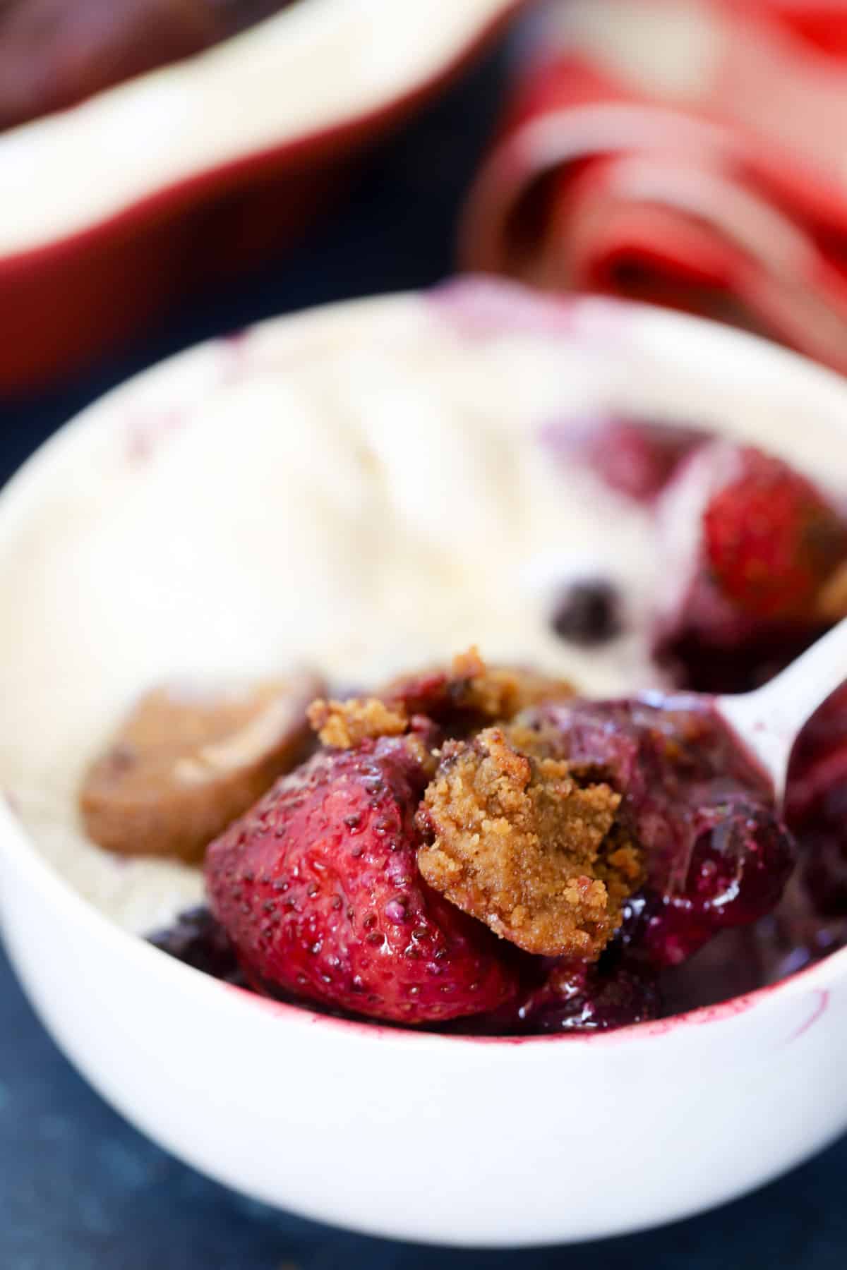 Close-up spoonful of berry crumble with a soft cookie chunk and juicy strawberry over vanilla ice cream