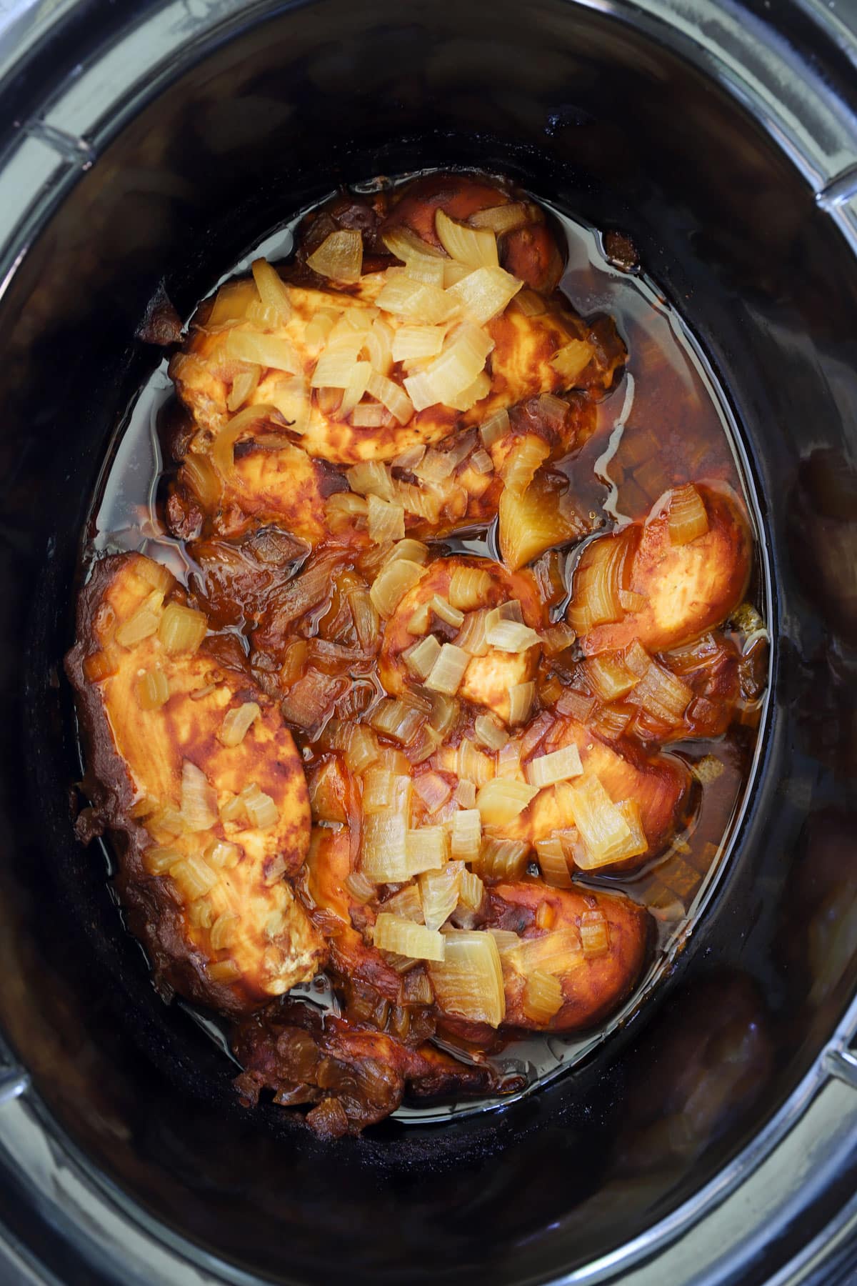 Cooked barbecue chicken breasts and thighs with softened onions in a slow cooker after cooking on low